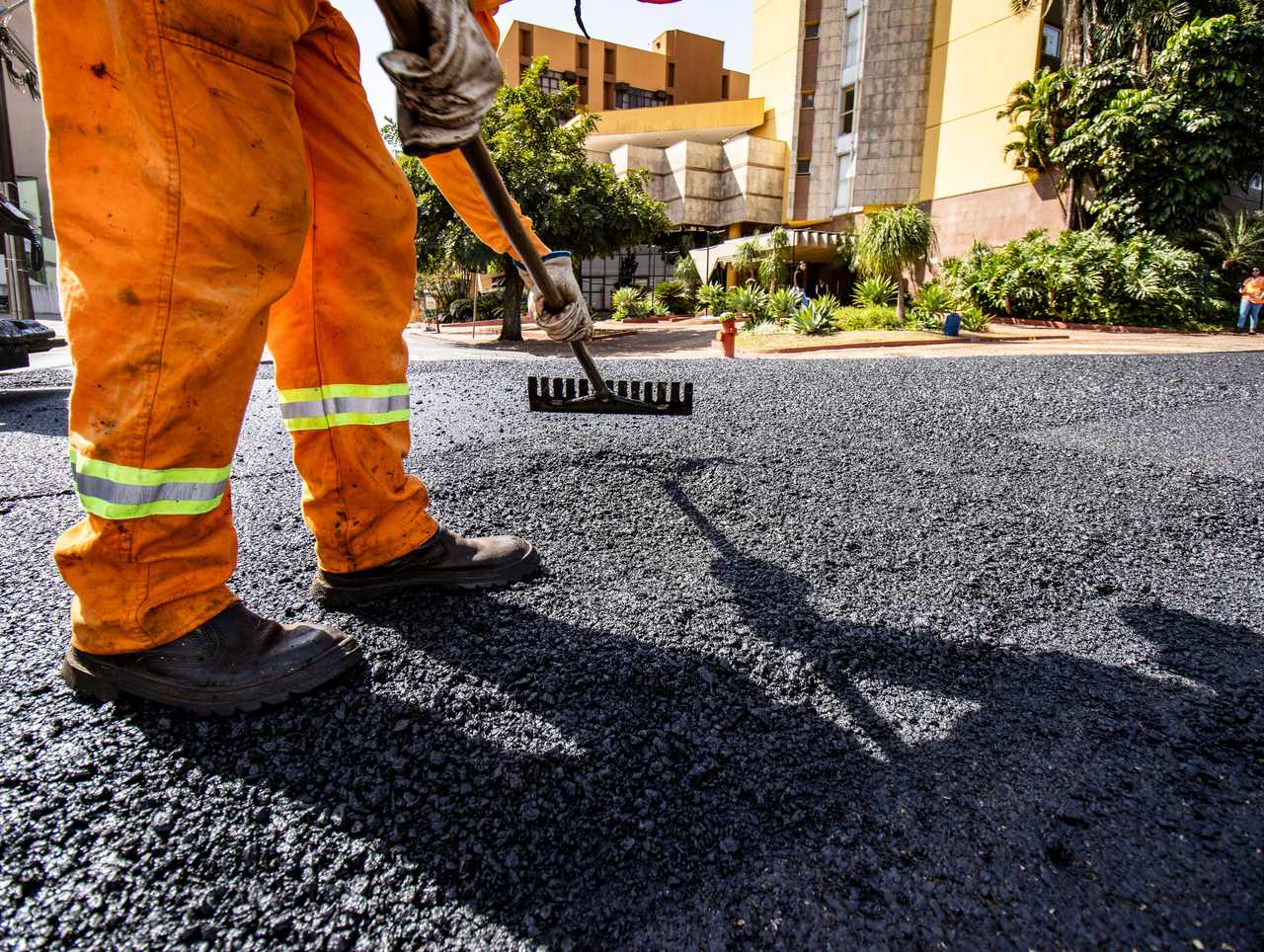 Paving worker raking fresh hot mix asphalt across a commercial lot