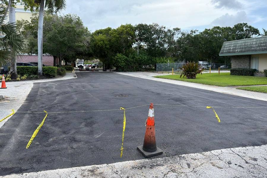 Freshly paved asphalt drive at a commercial property, taped off with cones while the new surface sets