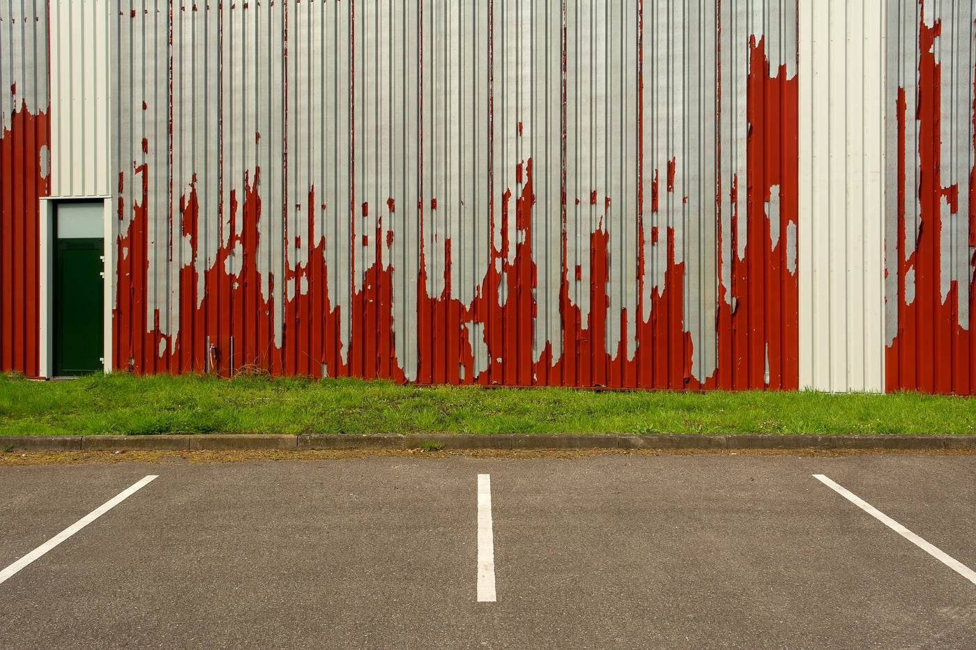 Sun-faded building wall beside a parking lot with oxidized grey asphalt and worn stall lines